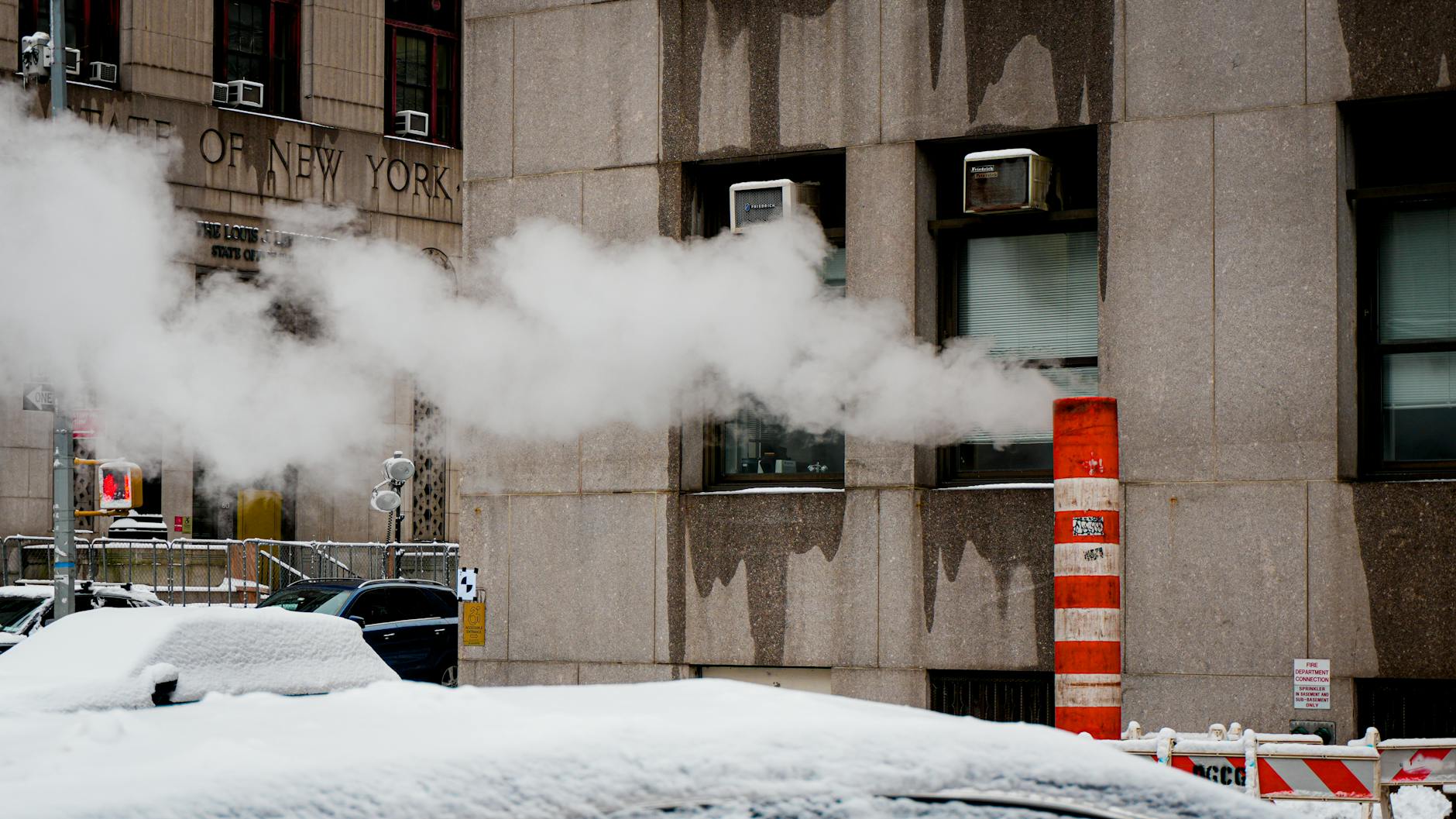 Snow-covered street in New York City with steam emerging from a vent against a building.