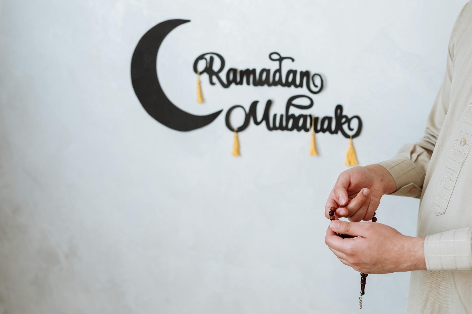 A Muslim man holding prayer beads with a Ramadan Mubarak wall decoration symbolizing the festive season.