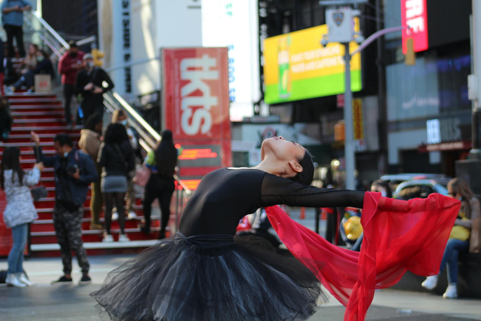 A graceful ballet dancer performs with a red scarf in Times Square, capturing movement and energy.