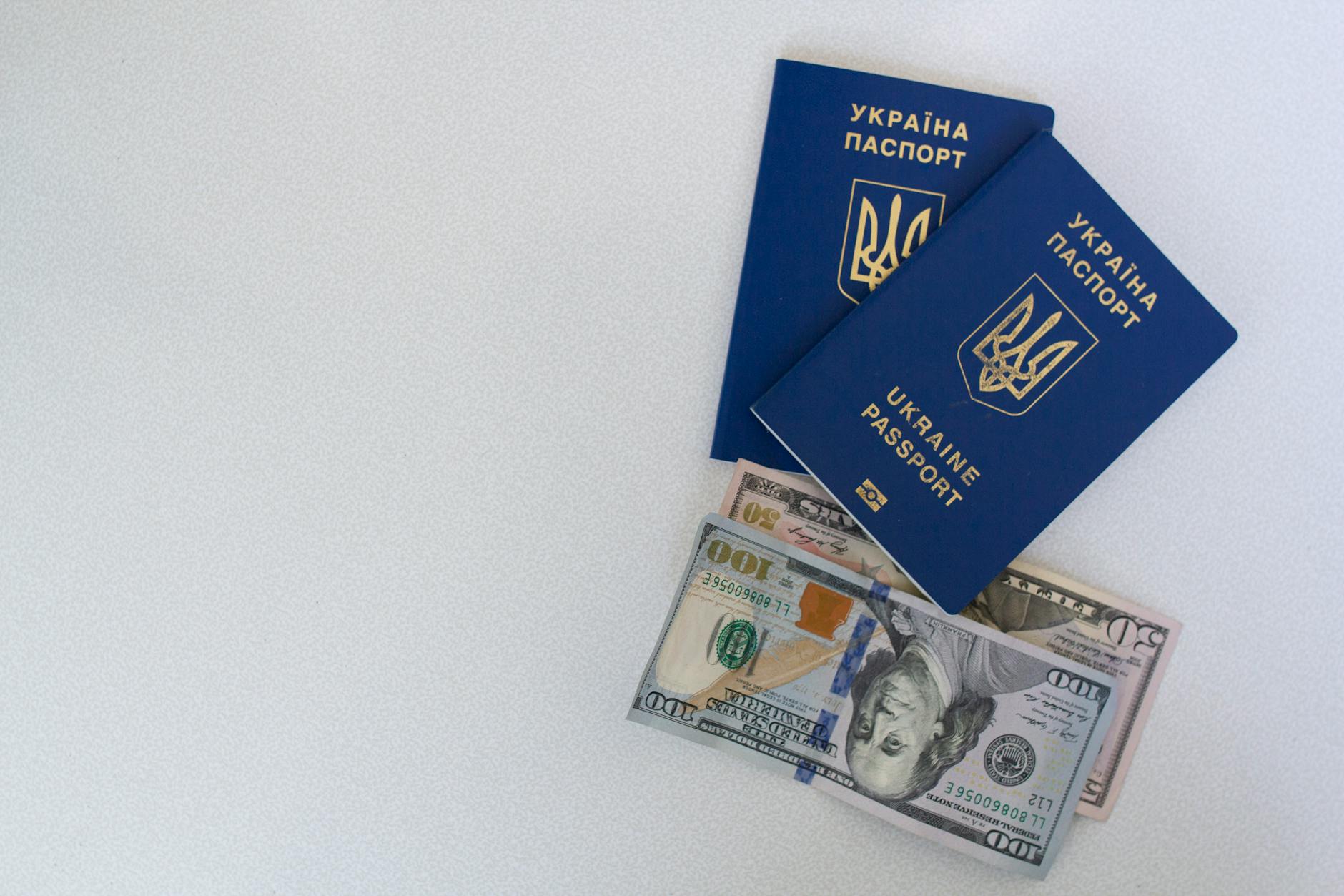 Top view of two Ukrainian passports with US dollar bills on a white surface.