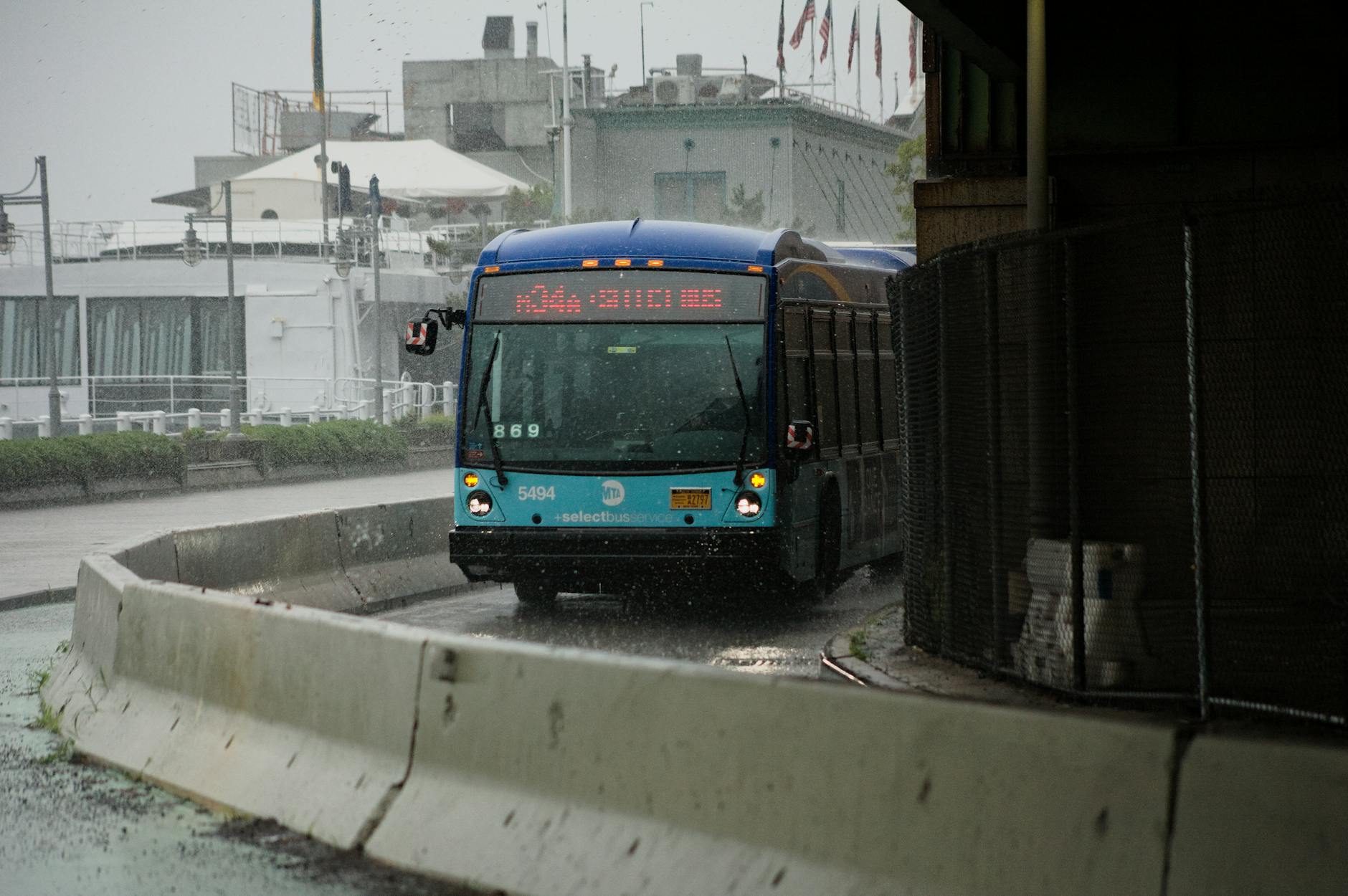 City bus navigating wet urban streets amidst heavy rain, showcasing public transportation in action.